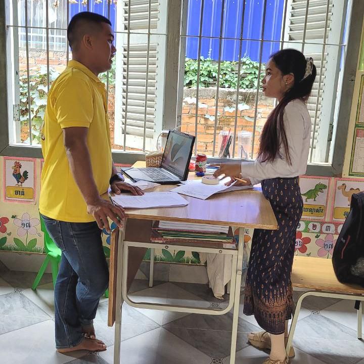 A project staff member and a teacher check a laptop at a school during the first follow-up visit