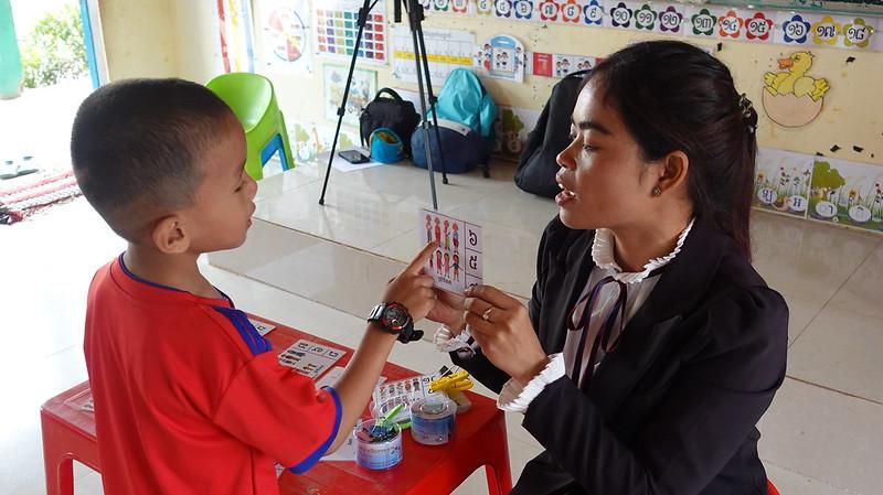 A teacher shows a flash card to a young boy in a decorated preschool classroom