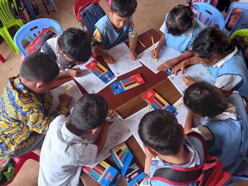 Preschool children color worksheets together with colored pencils around a table