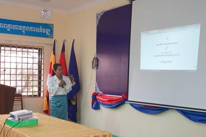 A woman presents the baseline survey results beside a projector screen at the kick-off meeting