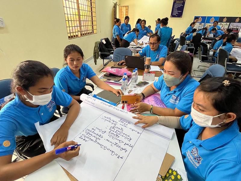 Teachers wearing masks write a simple lesson plan together on a large sheet of paper