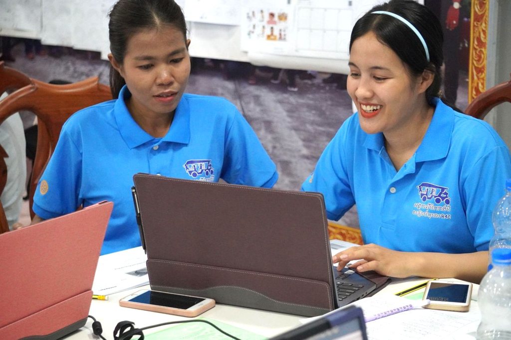 Two teachers in blue shirts work together at a laptop during the second workshop computer lesson