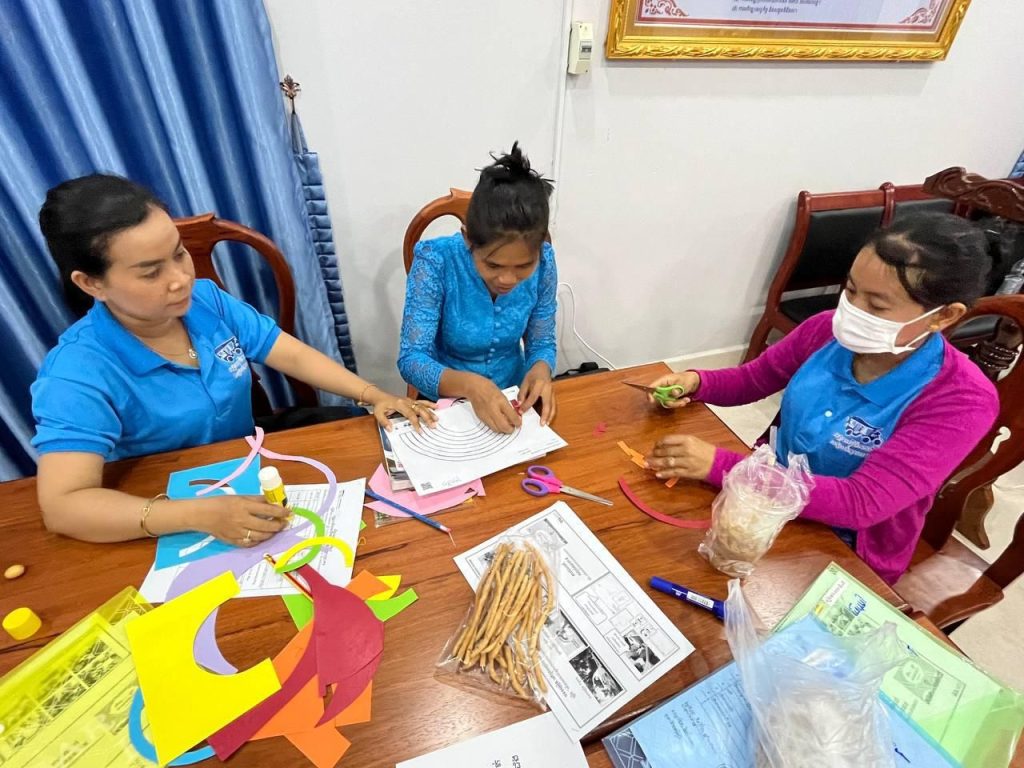 Teachers sit around a table covered with colored paper and worksheets, trying out the materials
