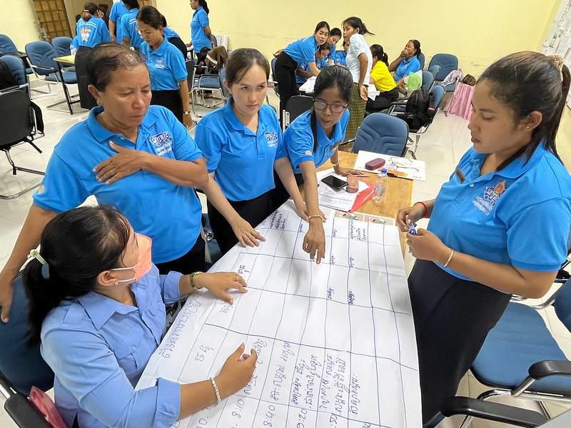 Teachers gather around a large sheet of paper to practice writing a lesson plan