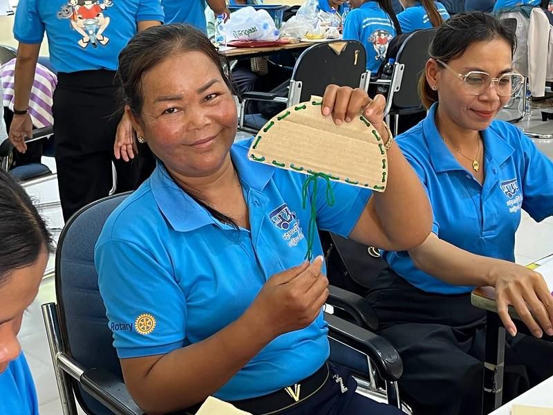 A smiling teacher holds up a woven craft fan she made at the workshop