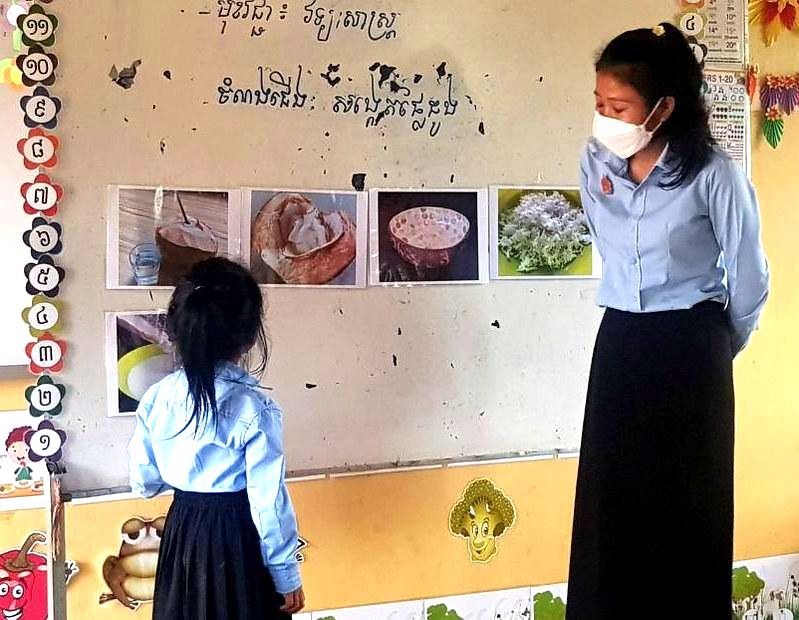 A teacher and a girl look at a wall display of pictures during a lesson