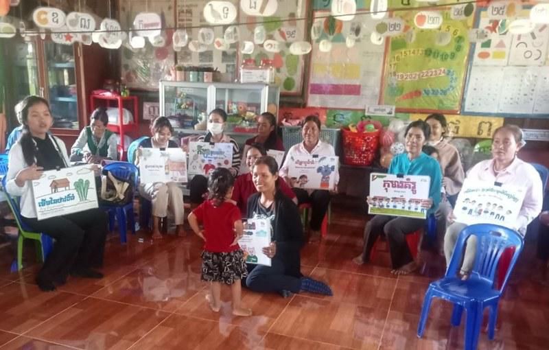Teachers seated in a circle hold up Kamishibai picture cards in a classroom during the meeting