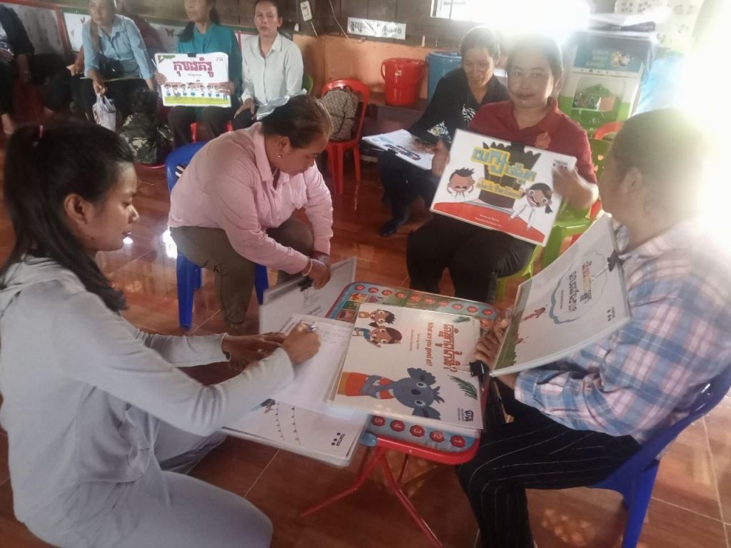 Teachers sit on the floor looking at a Kamishibai and storybook together during the meeting