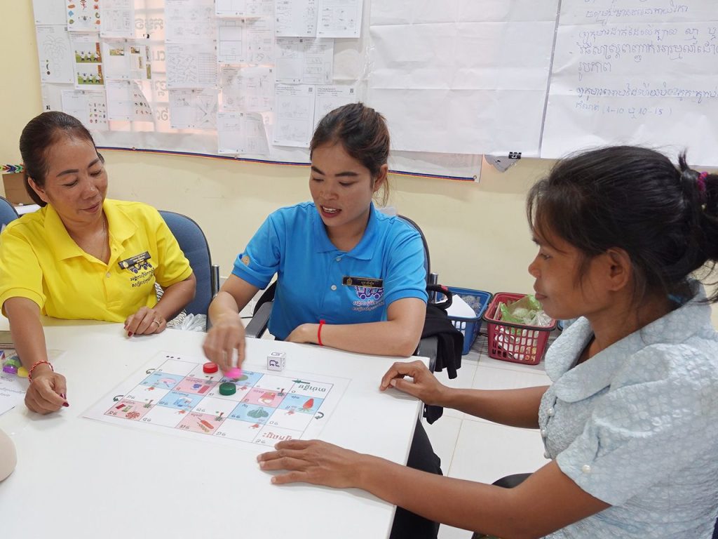 Teachers in blue and yellow shirts play a board game together around a white table