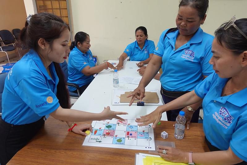 Teachers play a board game together at a table with dice and game pieces
