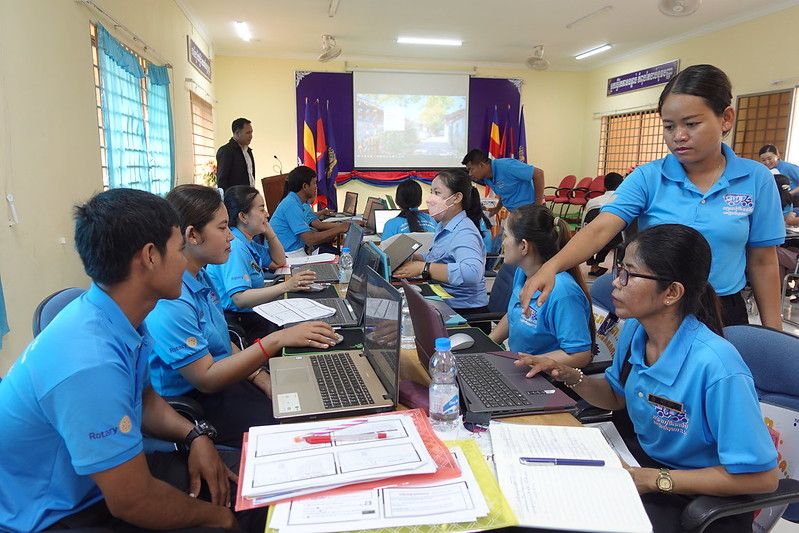 Teachers in blue shirts practice Microsoft Word on laptops in a training room during the workshop