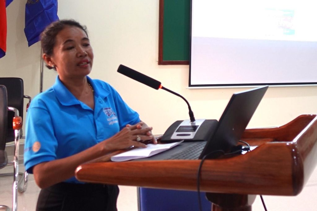 A teacher speaks at a wooden lectern with a laptop and microphone during the workshop