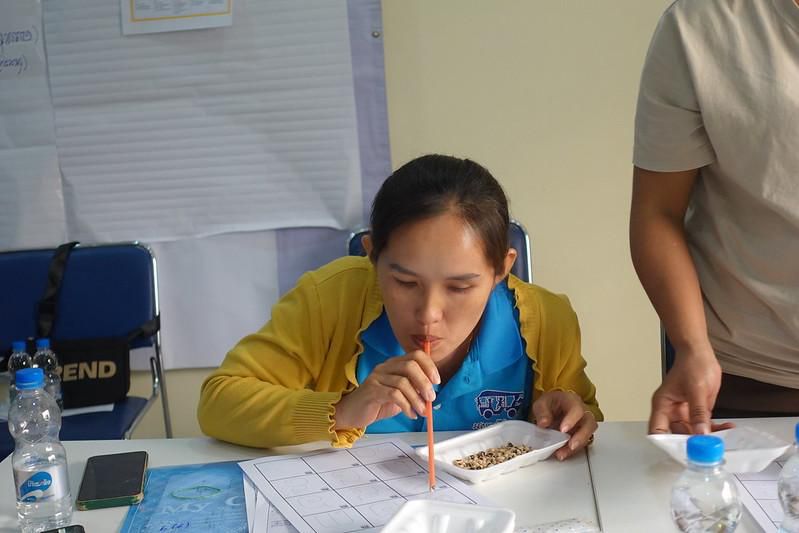 A teacher in a yellow cardigan blows through a straw to move seeds across a tray