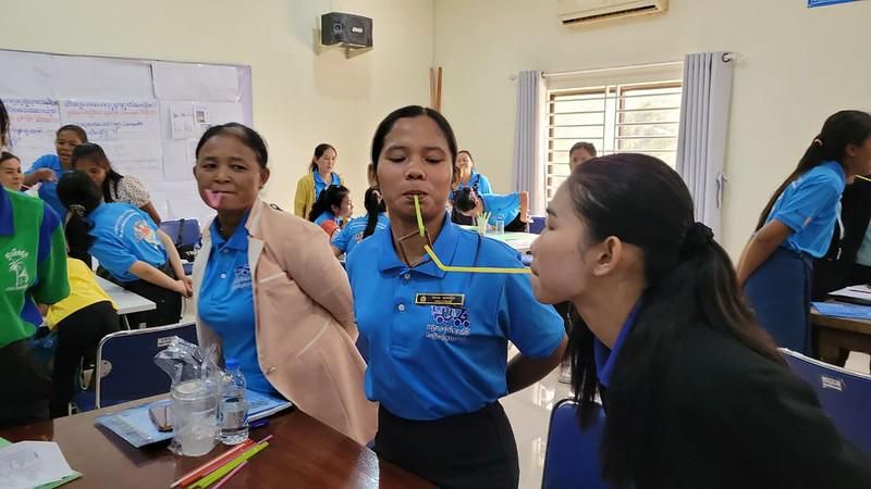 Two teachers play an activity game, passing a drinking straw from mouth to mouth