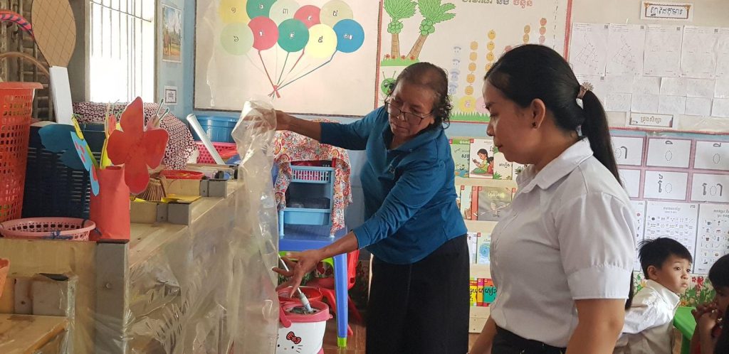 A teacher and a visitor look over classroom display materials and play corners during a classroom environment assessment