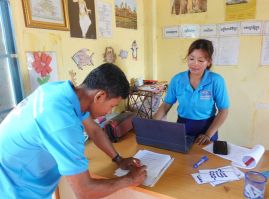A project staff member and a teacher work at a desk with a laptop and papers during a school visit