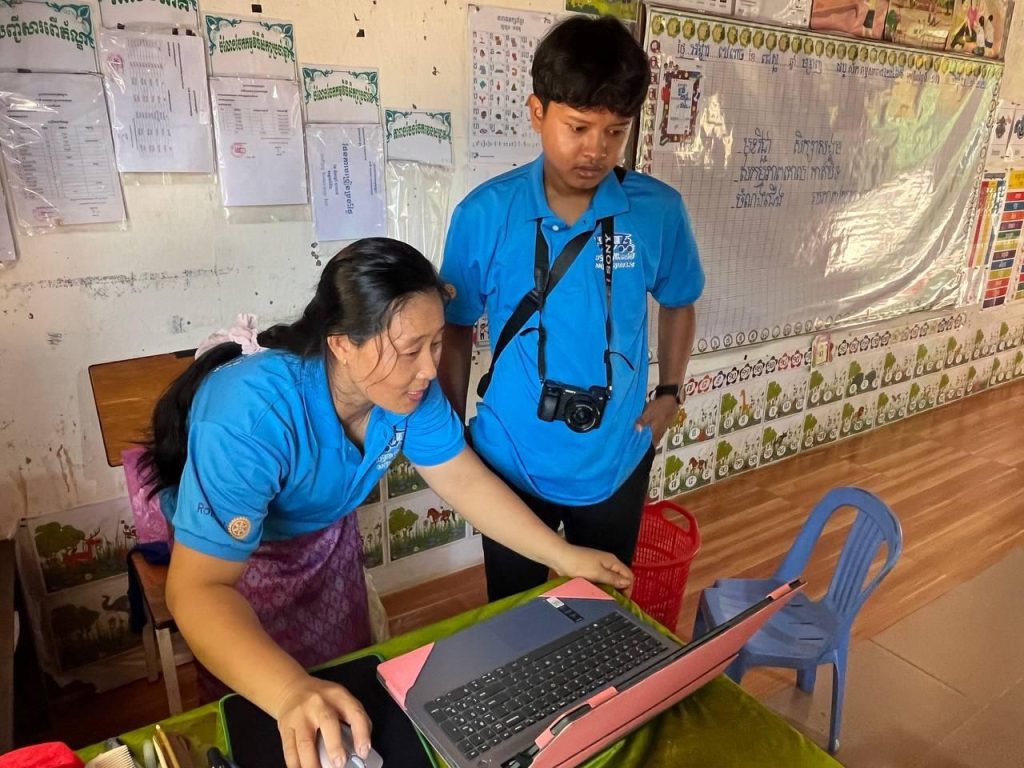 A teacher and a project staff member with a camera look at a laptop screen in a classroom