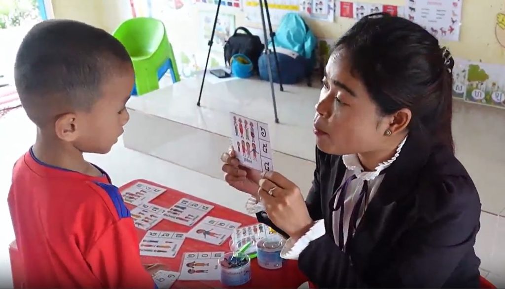 A teacher uses family cards from the resource package with a young child at a classroom table