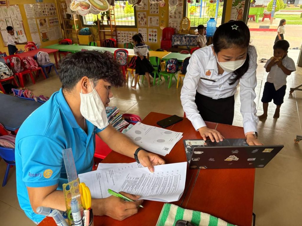 A project staff member and a teacher go through papers at a laptop during a school visit