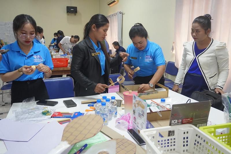 Teachers make paper and cardboard crafts at a table covered with materials during the workshop
