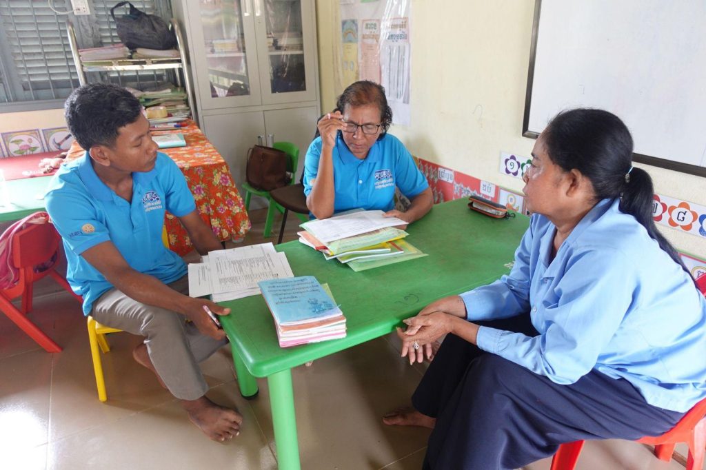 Two assessors and a teacher sit at a green table going through books and papers