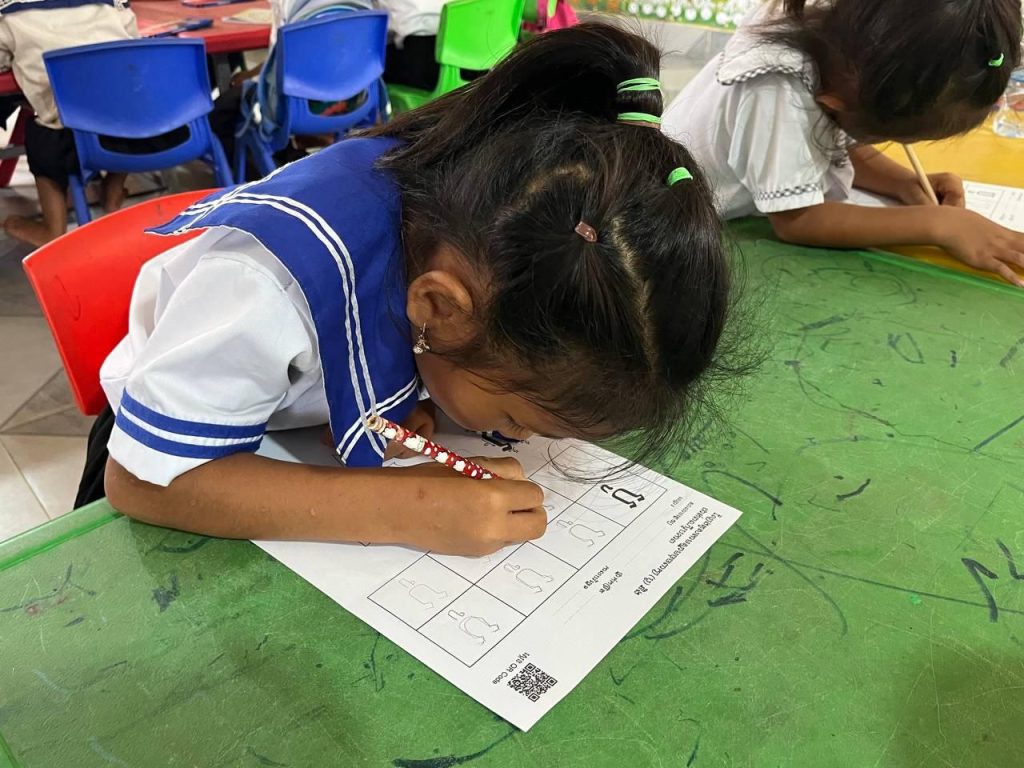A girl in a school uniform writes on a worksheet at a green table