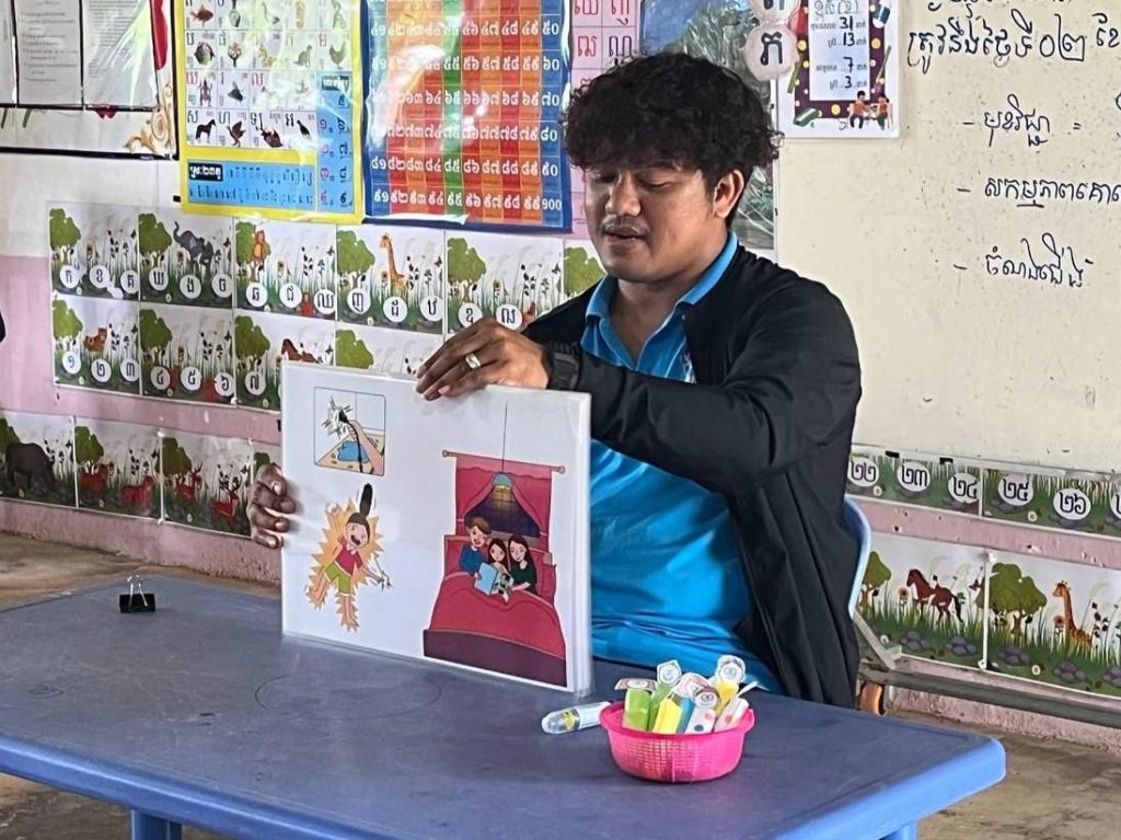 A teacher holds up an illustrated picture board while telling a story at a classroom table