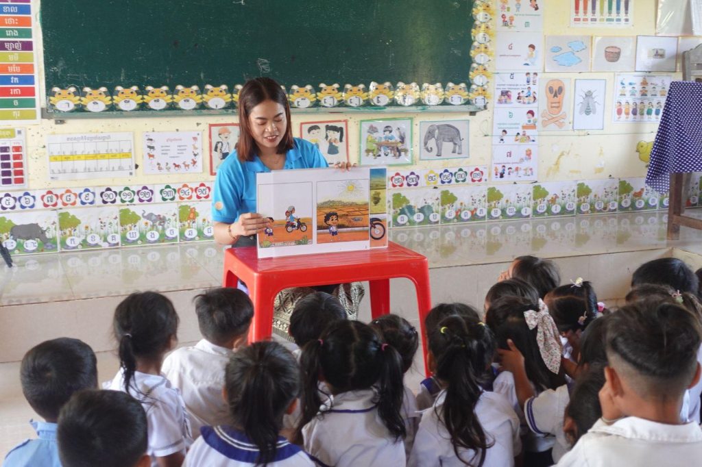 A teacher reads a picture story to a group of children gathered at the front of the classroom