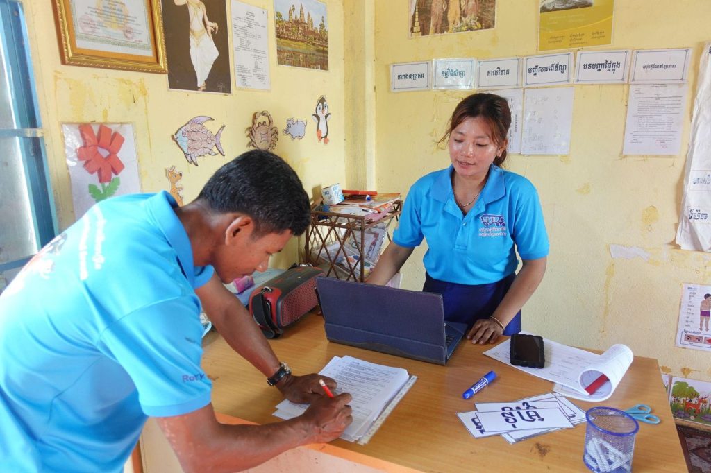 A project staff member writes notes with a teacher beside her laptop during a school visit
