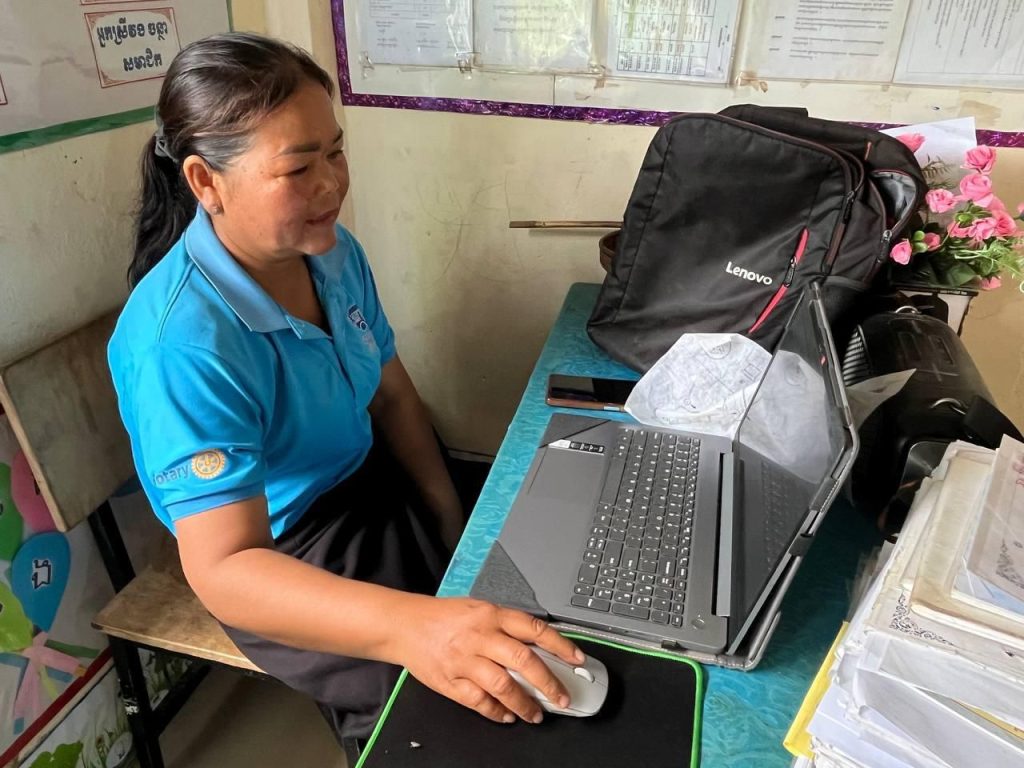 A teacher uses a laptop at her desk in a classroom during the follow-up school visit