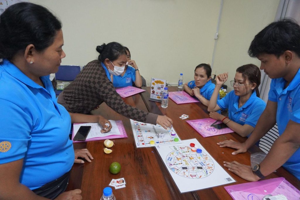 Teachers gather around a colourful board game on a wooden table at the workshop