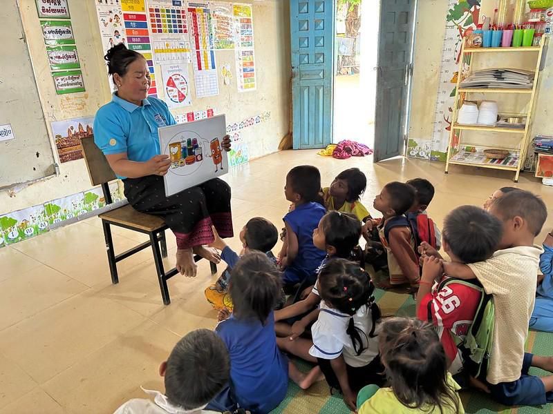 A teacher reads a picture book to children sitting on the floor of a classroom