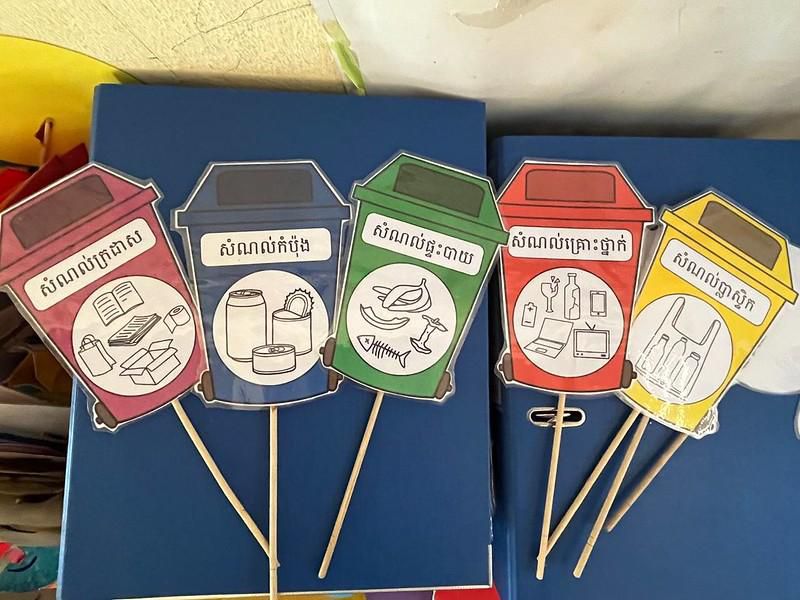 Colorful paper recycling bin crafts on sticks lie on a table