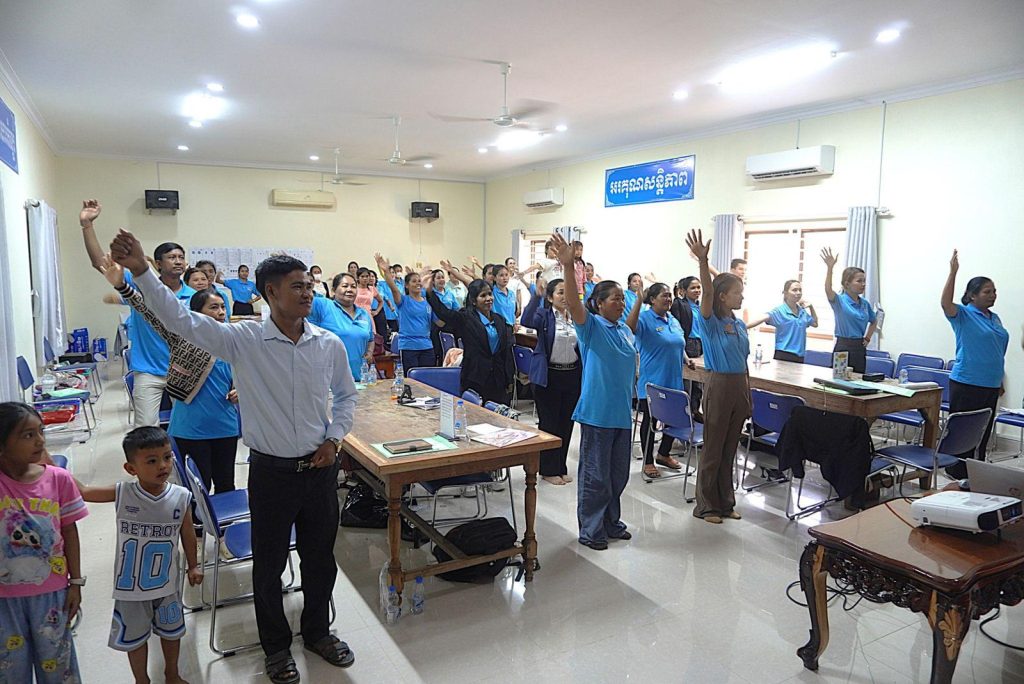 Workshop participants stand in rows with their arms raised during a full-body movement activity