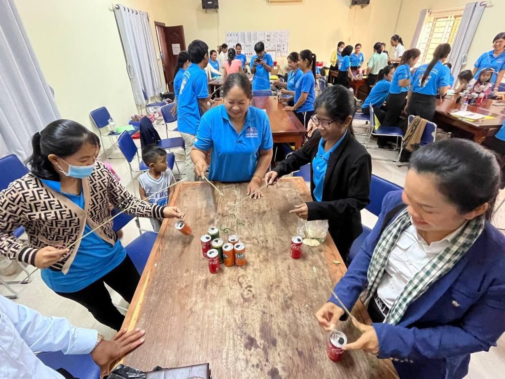 Teachers and a guest build a game from cans and cardboard tubes at a long table