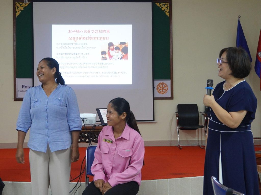 Teachers stand at the front beside the expert while a slide on child development is projected