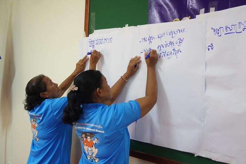 Two teachers write ideas on large sheets of paper hung on a wall