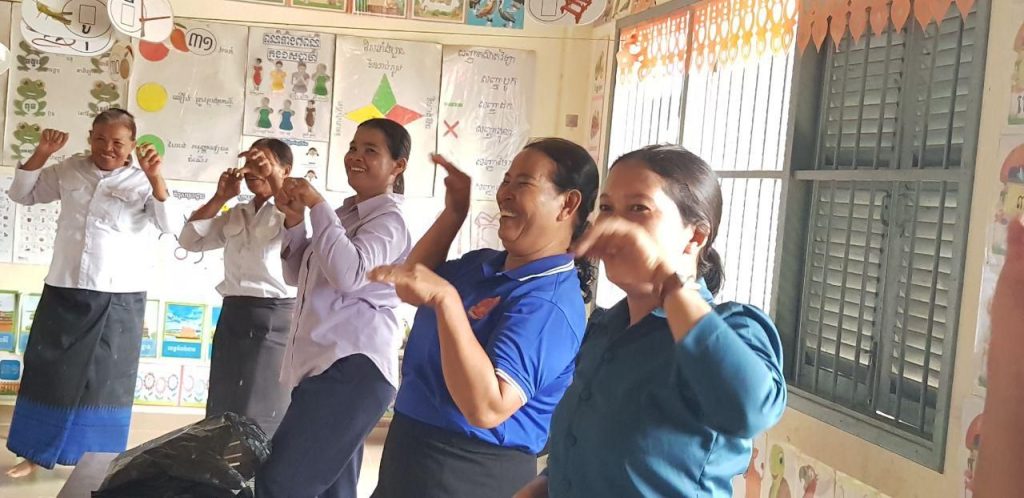 Teachers act out a hand-play activity together in a classroom during a technical meeting visit