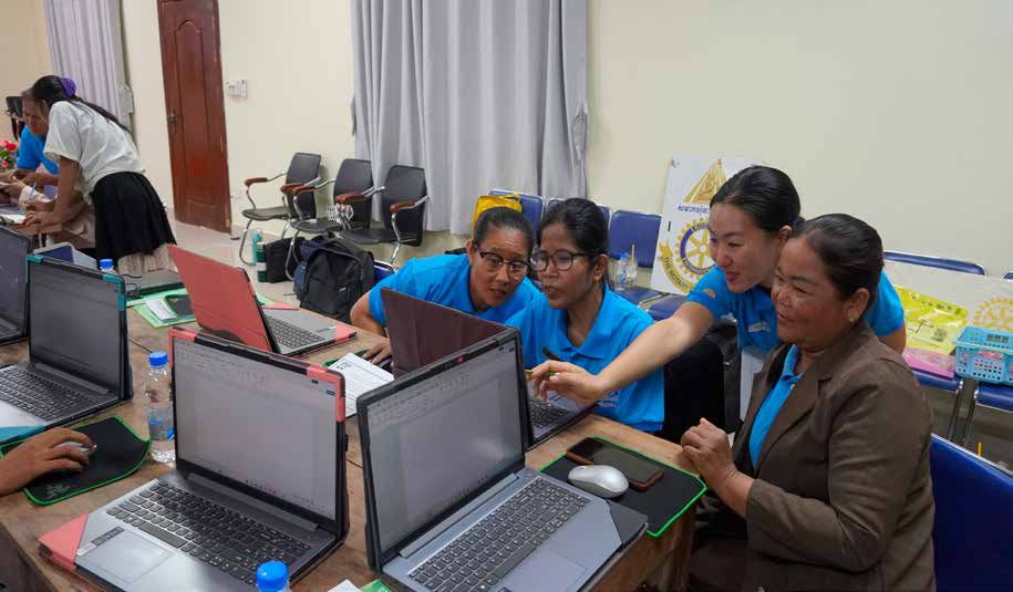 Teachers and a trainer sit at laptops in a training session, helping each other learn digital tools.