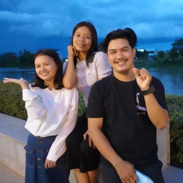 Three smiling TukTuk staff pose together by the river in the evening