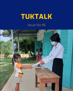 A teacher in a face mask hands a worksheet to a young girl at school
