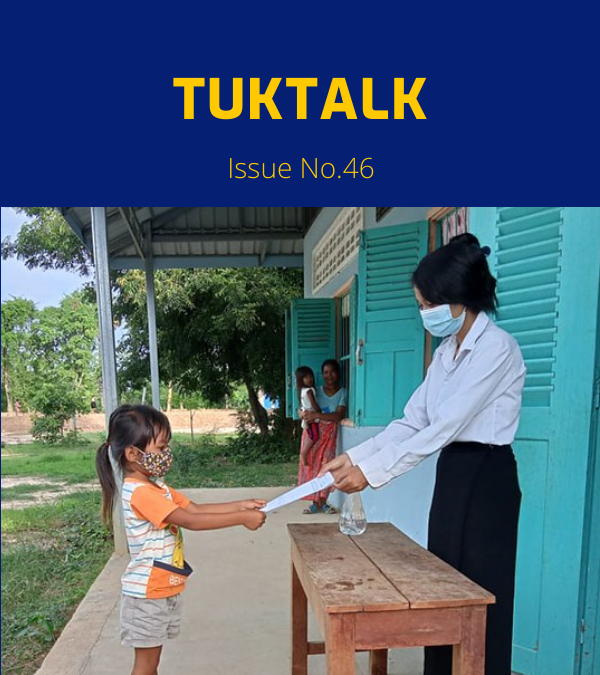 A teacher in a face mask hands a worksheet to a young girl at school