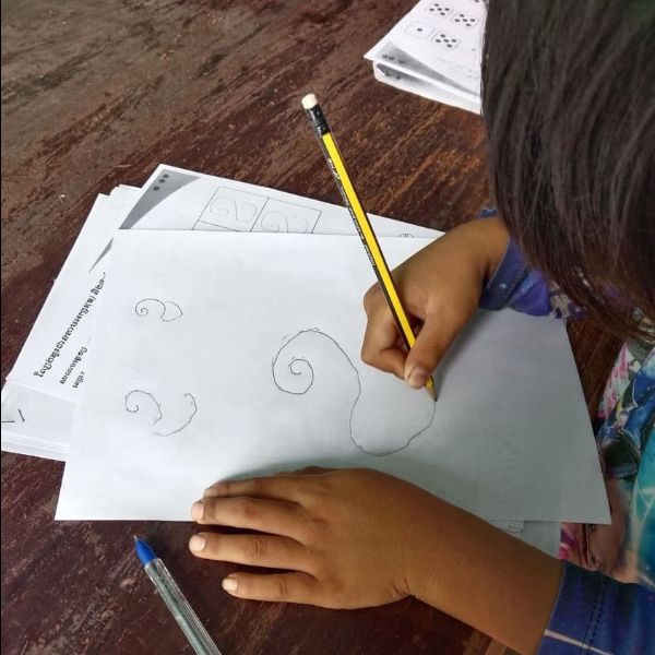 A child draws spiral patterns with a pencil on a TukTuk worksheet at a table