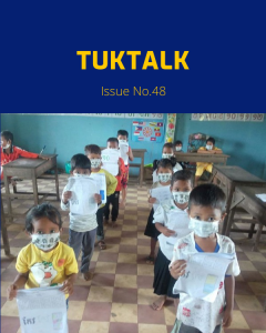 Masked kindergarten children walk in a classroom holding their worksheets