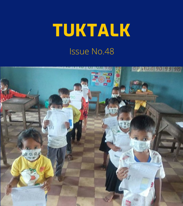 Masked kindergarten children walk in a classroom holding their worksheets