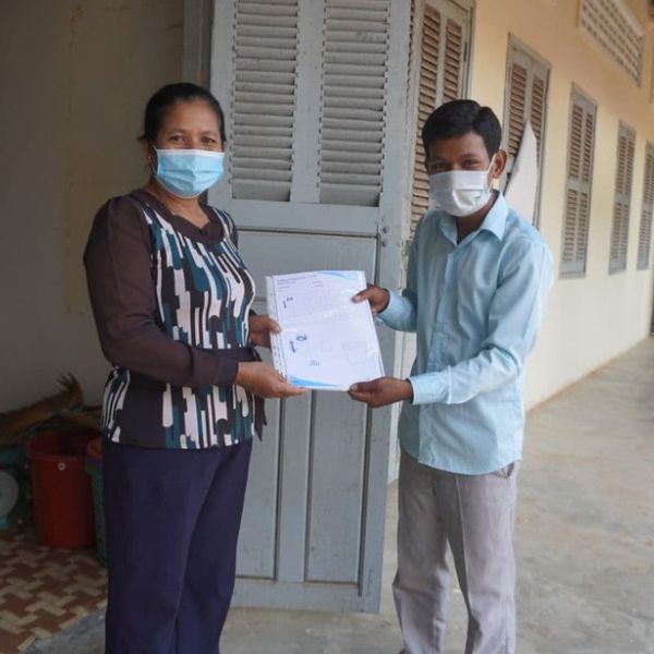 A man in a mask receives a worksheet from a teacher outside a school building