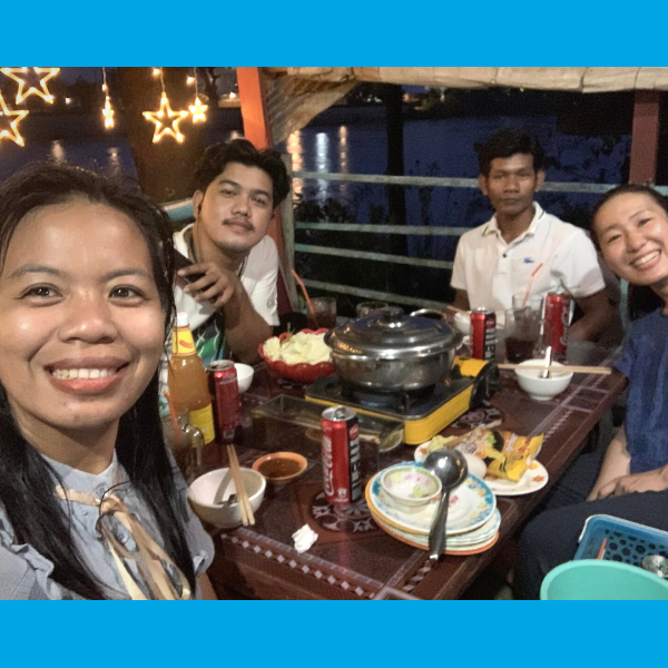 Four TukTuk staff smile around a hotpot dinner table in a riverside restaurant