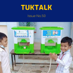 Two boys stand beside green hand wash stands at a school
