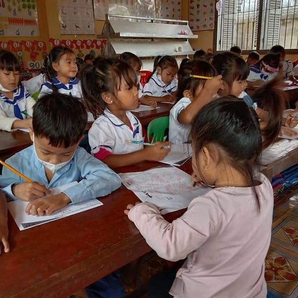 Preschool children in uniform write on worksheets at long wooden tables in a classroom