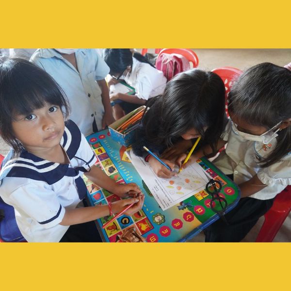 Three young children in uniform colour a worksheet together at a school table
